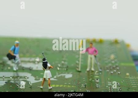 a female golfer on an electronic circuit board, in the background a man with a golf club bag and one with a flag Stock Photo