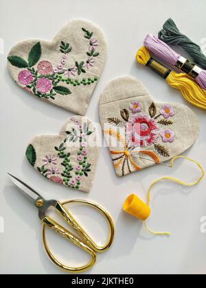 Fabric linen hearts with floral embroidery and vintage scissors, needle, thread on white, flat lay Stock Photo