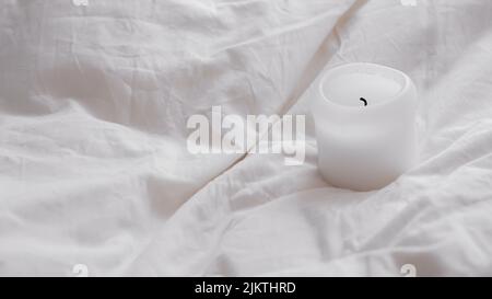 A closeup of a white candle on white crumpled sheets Stock Photo