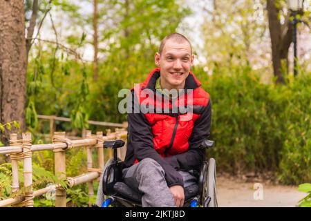 Portrait of a paralyzed young man in a public park in the city. Sitting in the wheelchair smiling Stock Photo