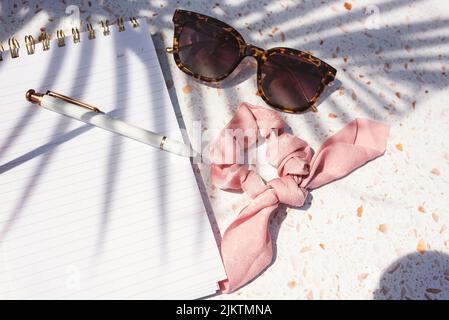 A top view of sunglasses and a scrunchie on a notebook in sunlight Stock Photo