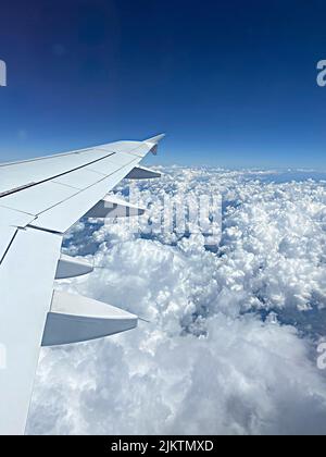 A vertical aerial of white fluffy clouds in the blue sky seen from an airplane window Stock Photo