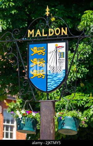 Maldon market town sign, with town coat of arms featuring lions and an east coast sailing barge on the River Blackwater. Hanging baskets. Picturesque Stock Photo