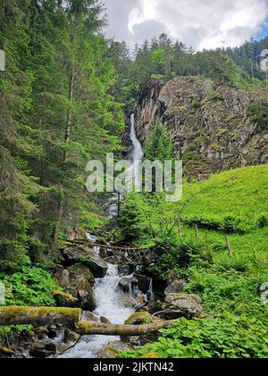 A vertical shot of a waterfall flowing through the trees in the Austrian Alps Stock Photo