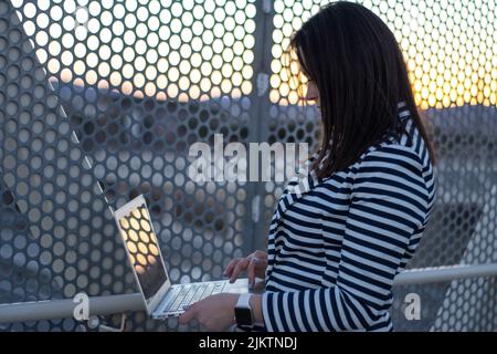 Smiling caucasian woman working outside on her computer on sunset Stock Photo