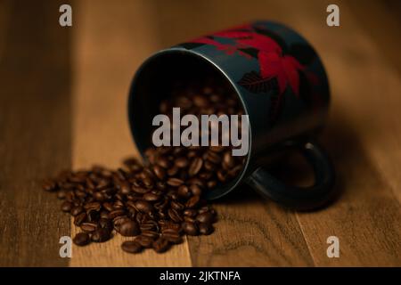 A closeup shot of a coffee beans spilling out of blue mug with red flower design on it Stock Photo