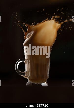 A vertical shot of a glass of karak tea splashed in the air on a black background Stock Photo