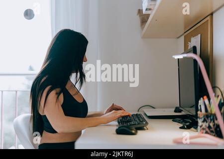 A young Hispanic woman sitting against a computer and typing on a keyboard. Stock Photo