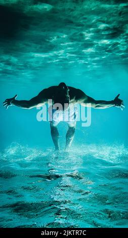 A vertical shot of a man upside down, swimming underwater Stock Photo