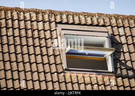 A closeup shot of a roof with brown tiles and an opened skylight window Stock Photo