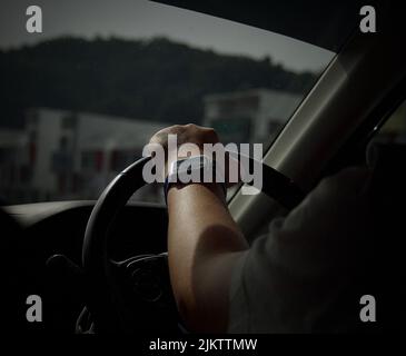 A back shot of a male with a watch driving a car holding the wheel with gray green mountains outside Stock Photo