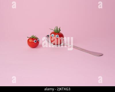 Two whole cherry tomatoes with eyes and a spoon isolated on a pink background Stock Photo