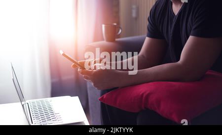 young man at home using his computer and phone having cup of coffee Stock Photo