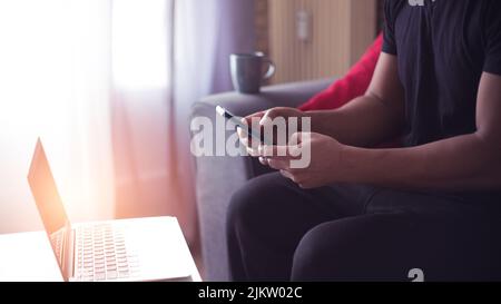 young man at home using his computer and phone having cup of coffee Stock Photo