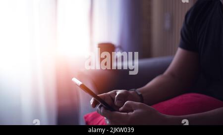 handsome young Hispanic at home drinking coffee and using his smart phone Stock Photo