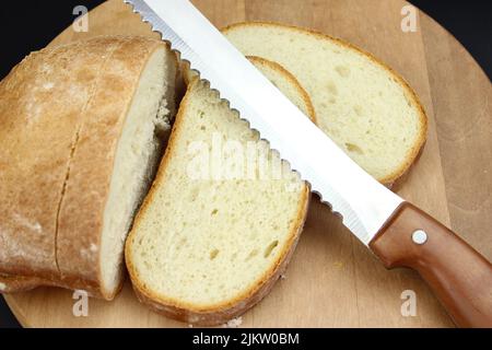 Whole grain bread put on kitchen wood board with a chef knife for cut on black background Stock Photo