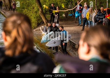 Surfers in Munich at the Eisbach river waiting to jump into the water. Popular destination, the surfers are watched by many people. Stock Photo