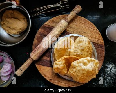 Stock photo of delicious hot deep fried puri or bhatura made up by wheat flour or all purpose flour kept in steel plate for serving. wooden rolling bo Stock Photo