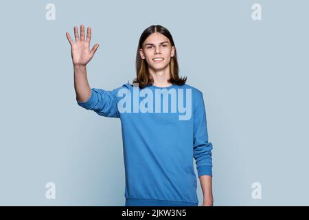 Young guy looking at camera waving his hand, on grey background Stock Photo