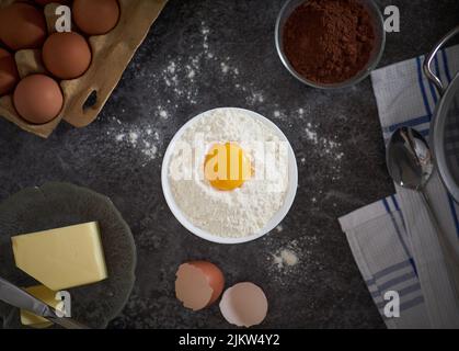 A top view of eggs and flour in a bowl, butter and chocolate powder on a table Stock Photo