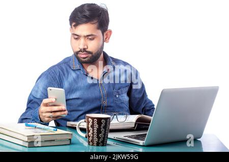 distracted man looking at mobile phone screen while working on laptop Stock Photo