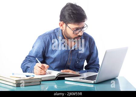 student writing on a notebook or diary while looking at laptop screen Stock Photo