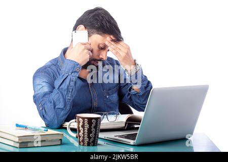tensed men talking on cell phone sitting in front of a laptop in white background Stock Photo