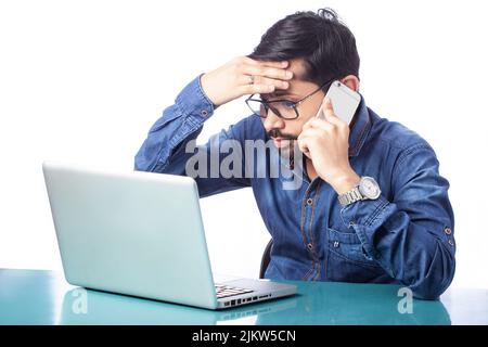 tensed man talking on cell phone and looking sadly at computer screen in isolated background Stock Photo