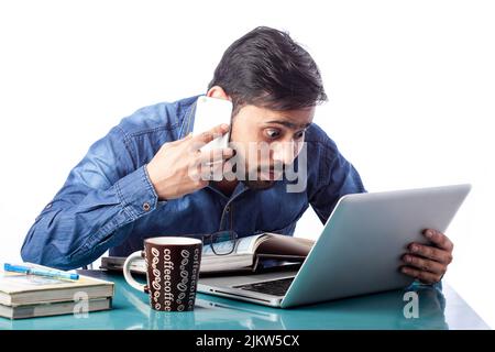 astonished businessman looking at laptop screen while talking on cell phone in isolated white background Stock Photo