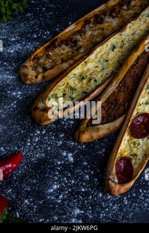 A vertical shot of four sticks of pide bread with cheese and meat on the black surface with flour Stock Photo