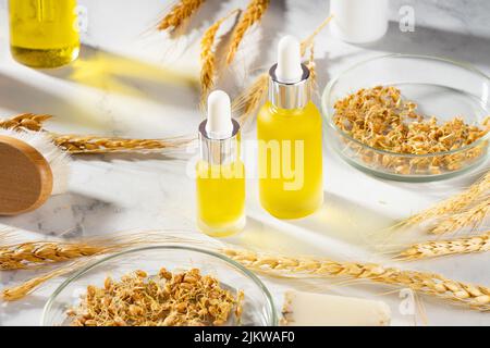 A conceptual composition of wheat essential oils, a bath brush and wheat germ on a marble table. Wheat serum oil for skin and hair care. Stock Photo