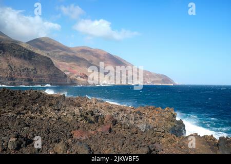 Volcanic coast of the island El Hierro against blue sea with big waves crashing to the shore, village Puerto de la Estaca, Canary Islands, Spain. Stock Photo