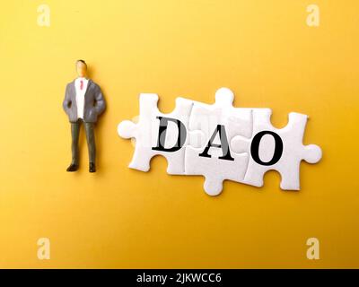 Miniature people and white puzzle with text DAO on yellow background. Stock Photo