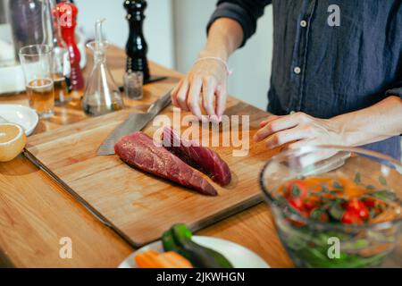 A closeup of the man cutting meat on the wooden board in the kitchen. Cooking concept. Stock Photo