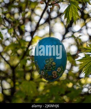 A vertical closeup of a decorative blue Easter egg hanging on the tree branch. Selected focus. Stock Photo