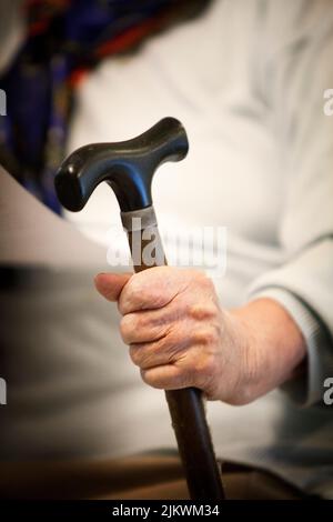 Elderly woman sits with her cane in a retirement home. Stock Photo