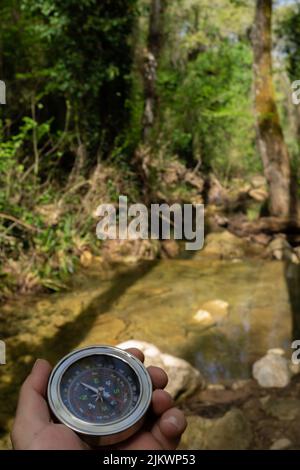 man's hand holding a compass in the forest with a mountain river in the background Stock Photo