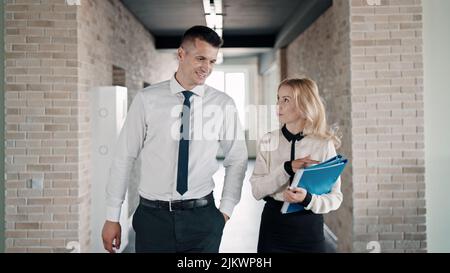 Two Caucasian co-workers talking and walking in an office Stock Photo