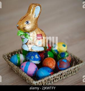 A closeup shot of a colorful painted easter eggs and chocolate bunny in straw basket on a wooden table Stock Photo