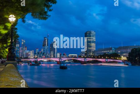 Lambeth Bridge lit up at nightfall in London, surrounded by modern skyscrapers in the Vauxhall and Lambeth districts of the city. Stock Photo