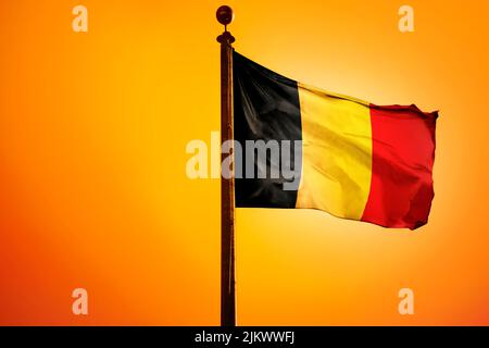 A digital illustration of the flag of Belgium waving against a bright yellow sky Stock Photo