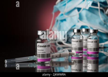 Close up of vaccine vials, anti covid and surgical masks on a black background with a red light. Stock Photo