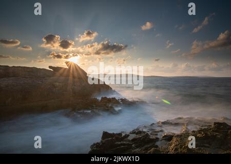 A beautiful scene of rocky cliffs with smoky seawater against a blue cloudy sky in Bugibba Bay, Malta Stock Photo