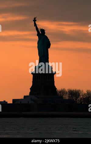 Silhouette of Statue of Liberty against a vivid orange sunset sky concept for NYC landmarks, American patriotism and symbol of freedom in America Stock Photo