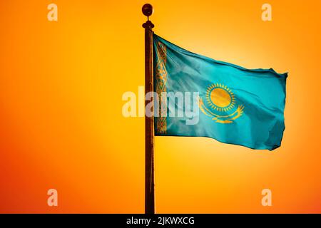 The national flag of Kazakhstan on a flagpole isolated on an orange background Stock Photo