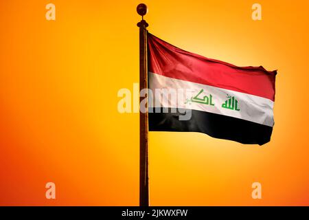 The national flag of Iraq on a flagpole isolated on an orange background Stock Photo