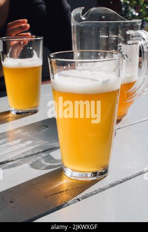 two glasses of beer on outdoor table with pitcher of beer and hand Stock Photo