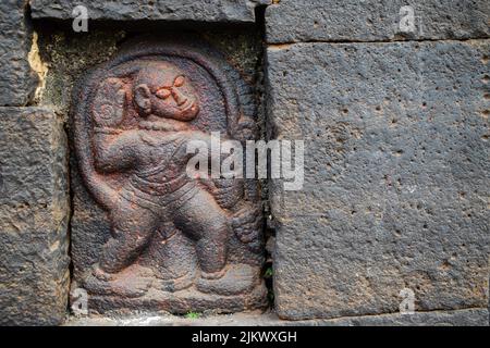 Stock photo of Ancient ruined archeological sculpture of hindu god hanuman engraved on gray stone wall. Picture captured during sunny day at Kolhapur Stock Photo