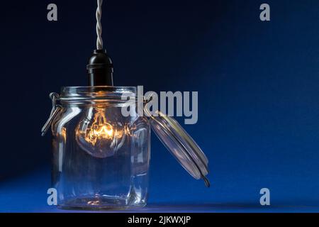 A lit incandescent light bulb enters a canning jar against a black and blue background. Stock Photo