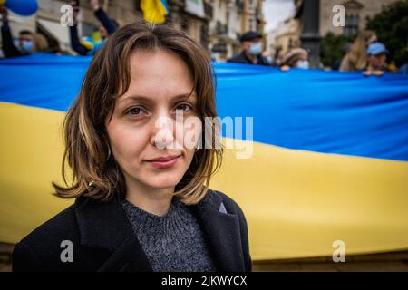 Ukrainian Refugee at Demonstration Against War with Russia Looking Optimistically at Camera with Giant National Flag in Background Stock Photo